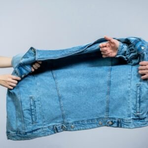 Two individuals pulling on a blue denim jacket, highlighting fashion and tension.